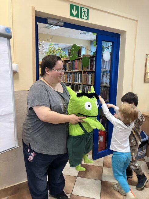 bibliotekarka trzyma dużą maskotkę, wokół niej dzieci