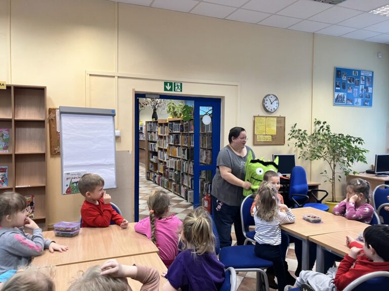 bibliotekarka trzyma dużą maskotkę, wokół niej dzieci