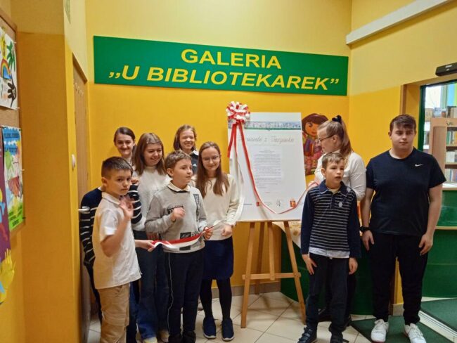 uczniowie zdejmują kotylion, uroczyście otwierając wystawę miniprzewodników po Targówku
