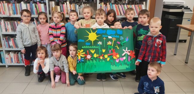 dzieci pozują z dużą wspólną pracą plastyczną - obrazem ze słońcem i kwiatami na łące