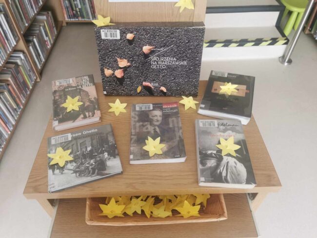 na stoliku w bibliotece są książki o powstaniu w getcie warszawskim, leżą na nich żonkile - symbole akcji