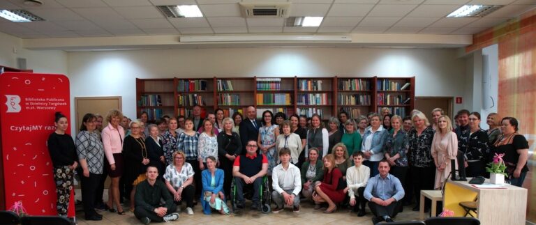 wszyscy pracownicy Biblioteki Publicznej na Targówku pozują do pamiątkowego zdjęcia na tle regałów z książkami