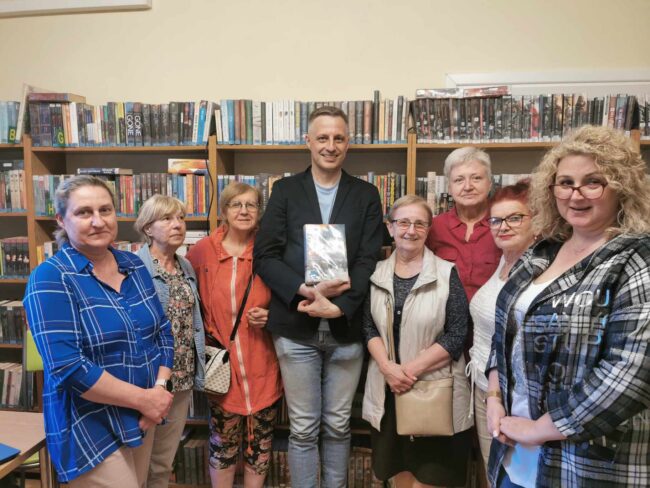 pamiątkowe zdjęcie Adama Stawickiego i uczestników spotkania w bibliotece