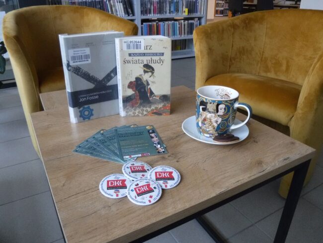 na stoliku książki, filiżanka i przypinki z logo Dyskusyjnego Klubu Książki