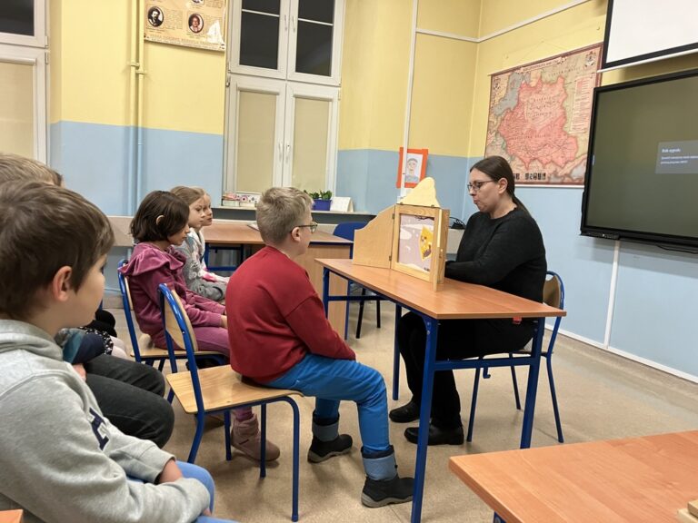 dzieci w sali lekcyjnej poznają bajkę prezentowaną w teatrzyku kamishibai