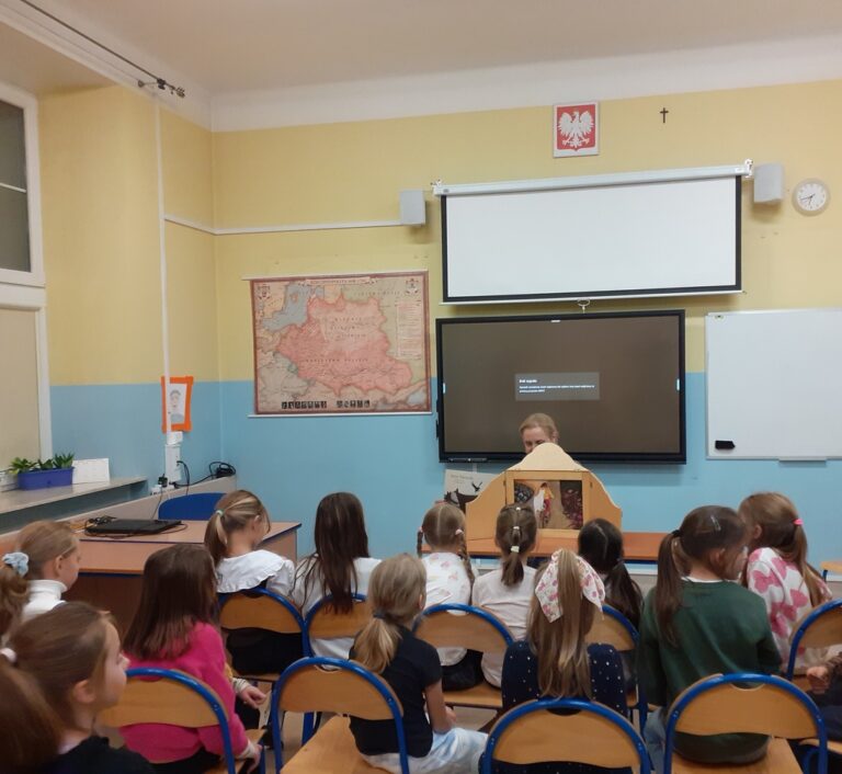 dzieci w sali lekcyjnej poznają bajkę prezentowaną w teatrzyku kamishibai