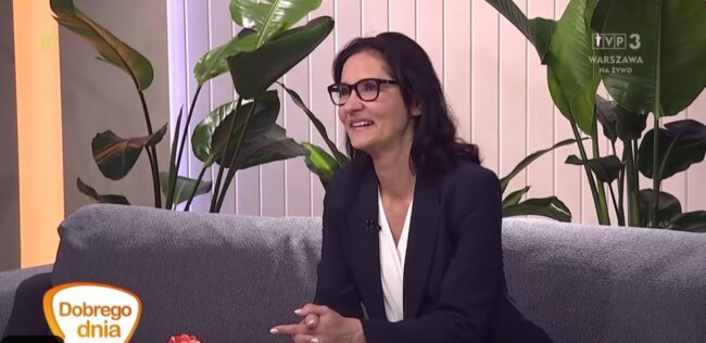 Zastępczyni dyrektora biblioteki na kanapie w studio TVP3 Warszawa; w tle duży kwiat doniczkowy