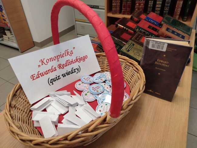 w koszyku wiklinowym kartka z napisem Konopielka quiz wiedzy i przypinki z logo biblioteki