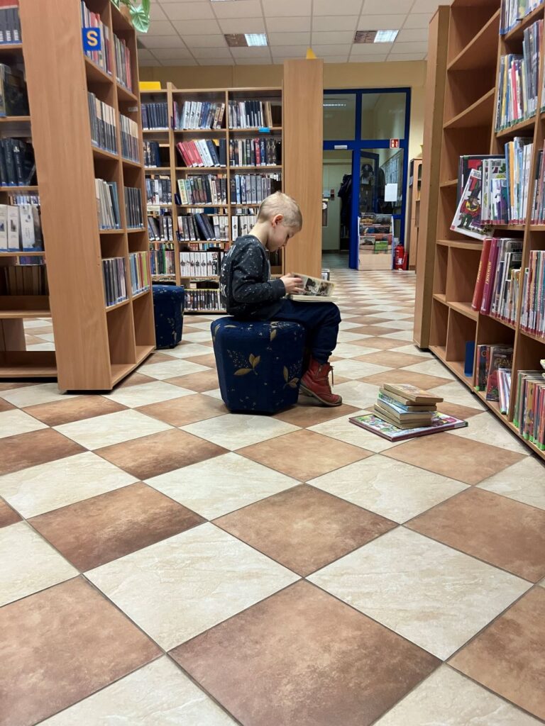 dziecko siedzi w bibliotece i czyta książkę