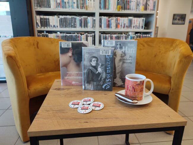 książki na stoliku, filiżanka, fotele, regał biblioteczny wypełniony książkami