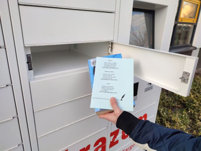 czytelnik wyjmuje ze skrytki książkomatu książkę z dołączonym wydrukiem wiersza Marii Pawlikowskiej-Jasnorzewskiej