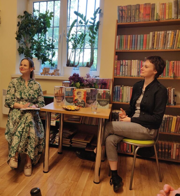 dwie kobiety siedzą przy stole podczas spotkania autorskiego