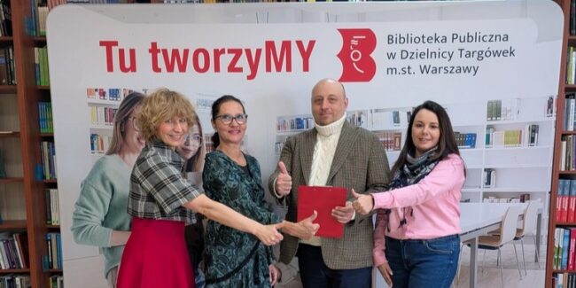 załoga biblioteki pozuje do zdjęcia na tle bannera z napisem Tu tworzymy