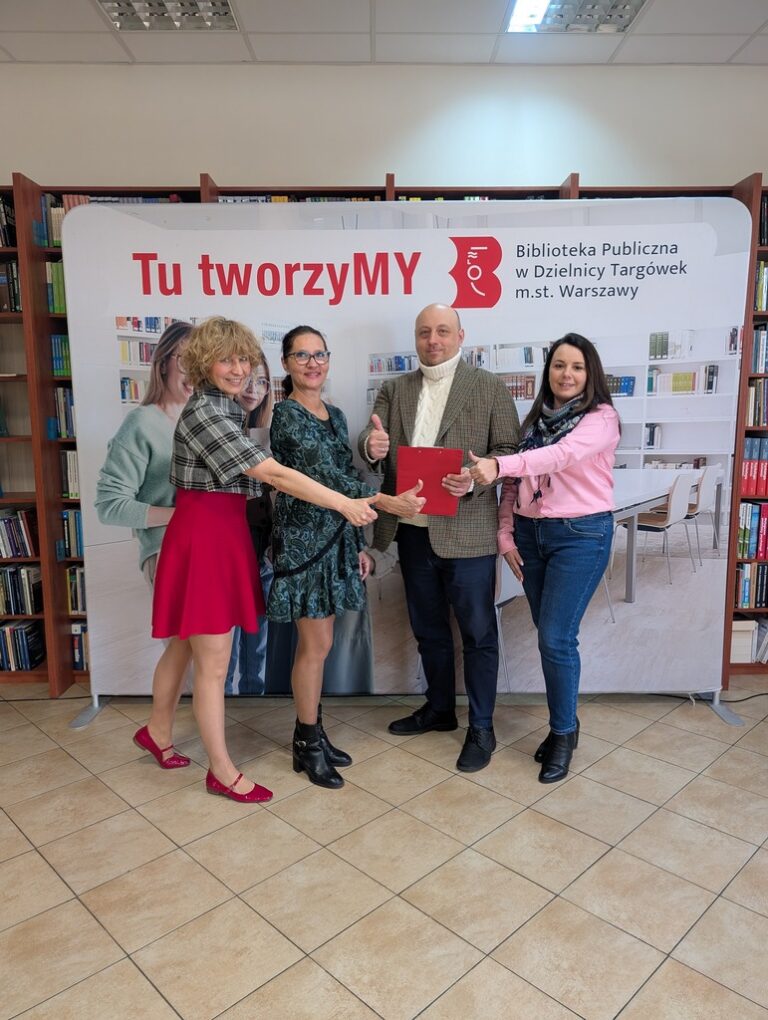 załoga biblioteki pozuje do zdjęcia na tle bannera z napisem Tu tworzymy