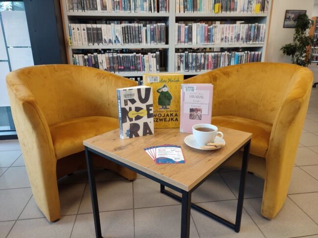 książki i filiżanka na stoliku, obok fotele, w tle regały wypełnione książkami