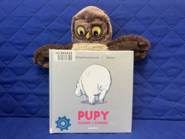 maskotka sowa Jadwiga trzyma skrzydłami polecaną książkę