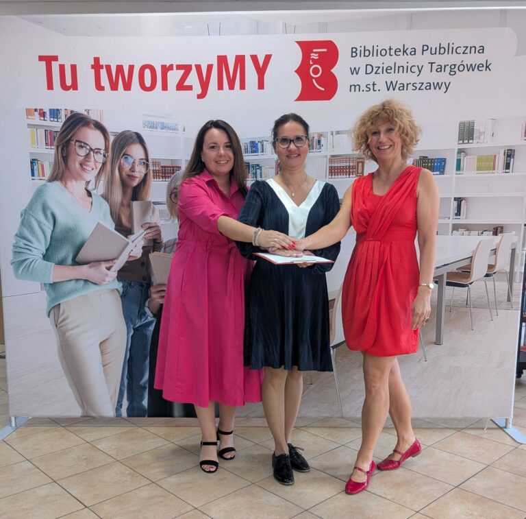 autorki projektu pozują do zdjęcia na tle ścianki ze zdjęciem biblioteki, logo biblioteki i napisem Tu tworzymy