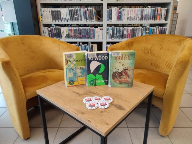 książki na stoliku, w tle fotele i regały biblioteczne