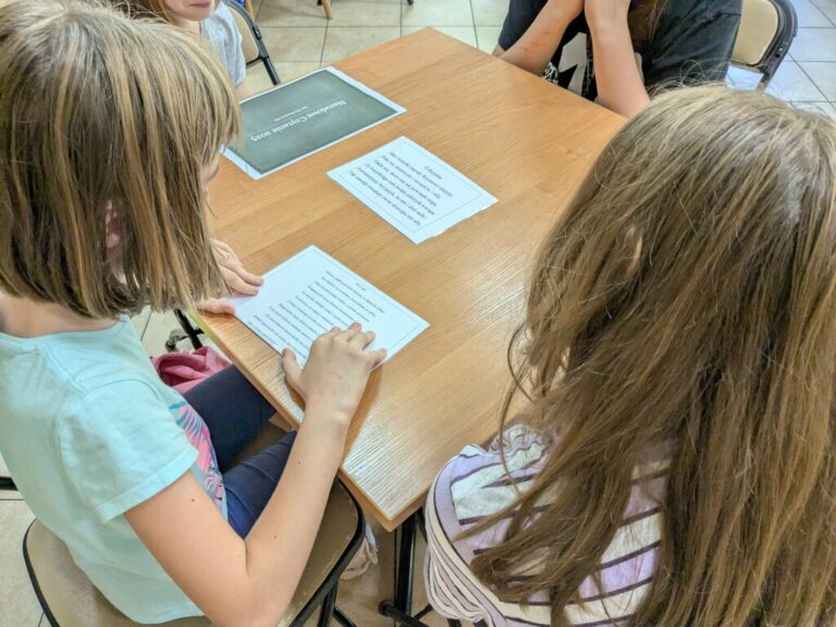 uczniowie szkoły podstawowej czytają w bibliotece fraszki Jana Kochanowskiego