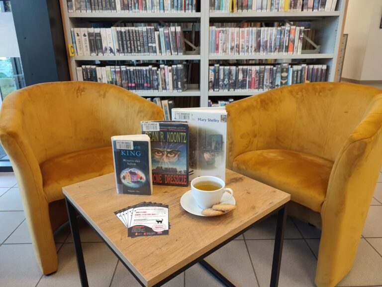 na stoliku książki omawiane podczas spotkania, a także filiżanka herbaty, w tle fotele i regały wypełnione książkami