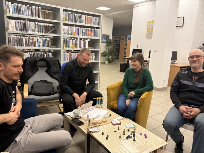 sesja RPG w bibliotece; kilka osób wokół stołu z planszą i pionkami