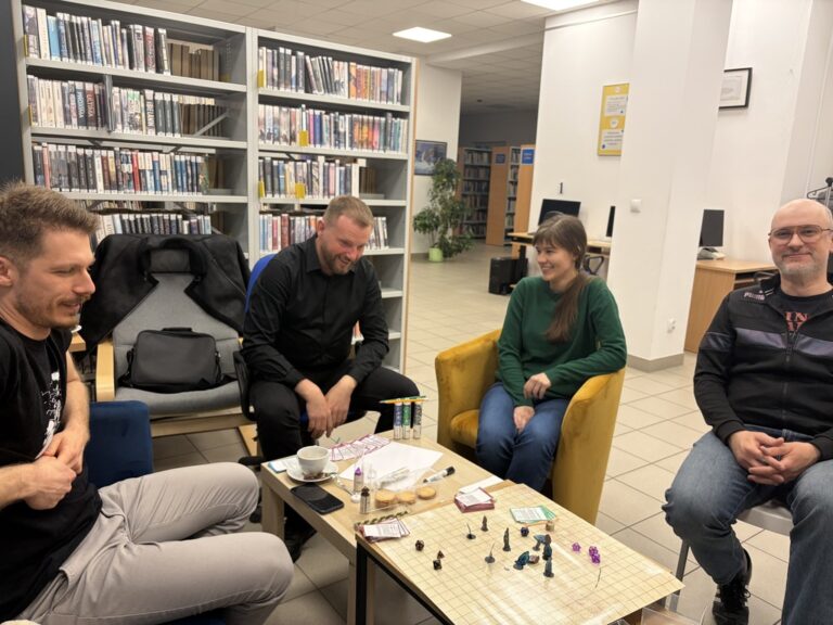 sesja RPG w bibliotece; kilka osób wokół stołu z planszą i pionkami