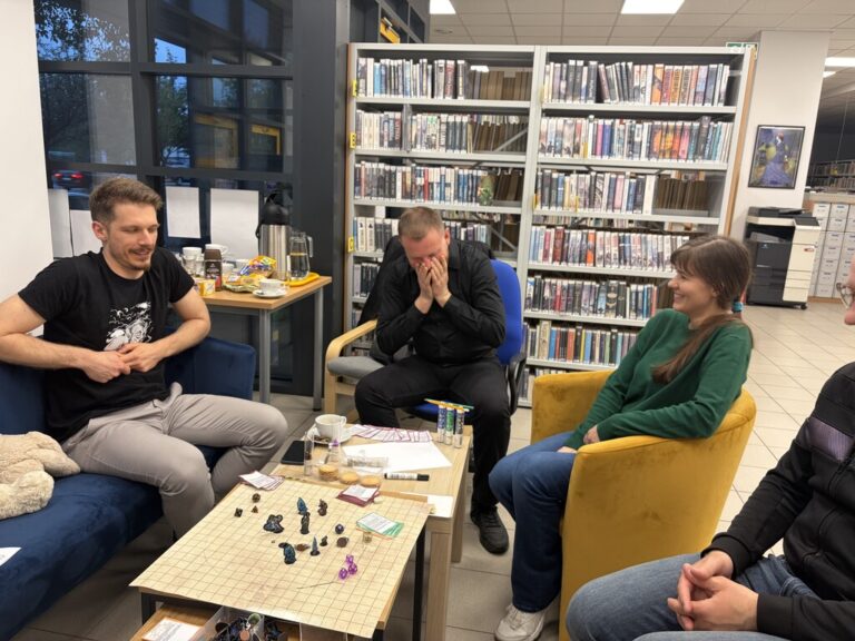 sesja RPG w bibliotece; kilka osób wokół stołu z planszą i pionkami