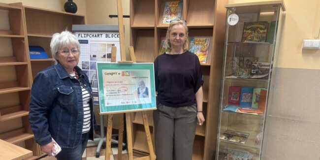 pisarka i kierowniczka biblioteki pozują do pamiątkowego zdjęcia przy plakacie promującym spotkanie
