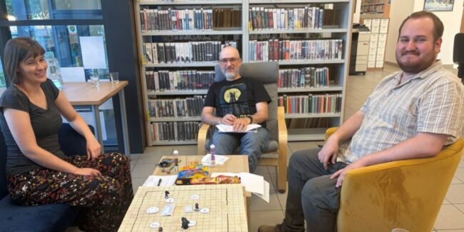 sesja RPG w bibliotece - 3 osoby przy stoliku grają