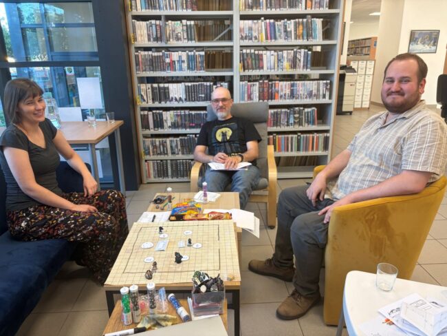 sesja RPG w bibliotece - 3 osoby przy stoliku grają