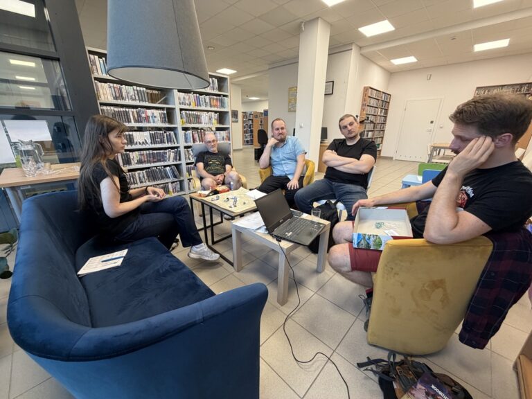 grupa osób siedzi przy stoliku w bibliotece i gra w RPG