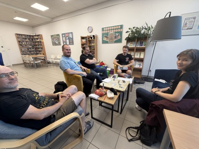 grupa osób siedzi przy stoliku w bibliotece i gra w RPG